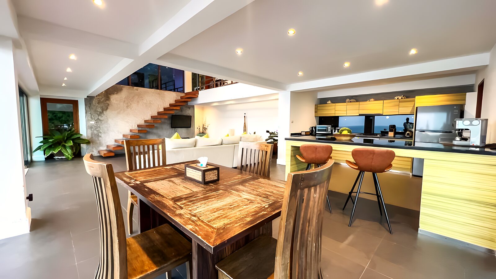Open-plan kitchen and rustic wood dining table under a high ceiling